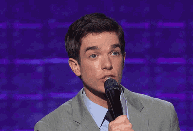 a man in a suit is holding a microphone and making a surprised face