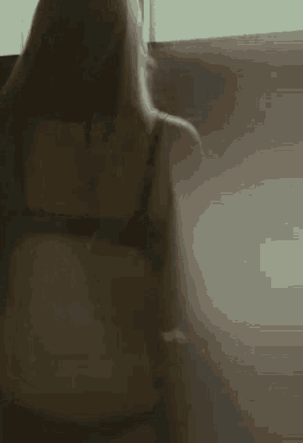 a woman in lingerie is standing in front of a window and looking out .