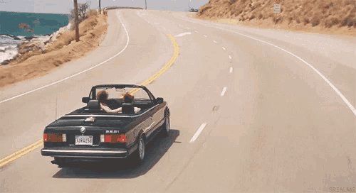 a man and woman are driving a convertible car down a highway .