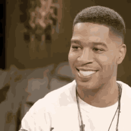 a man is smiling and looking at the camera while wearing a white shirt .