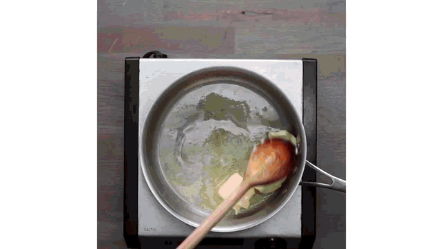 a wooden spoon is stirring butter in a pan on a stove top .