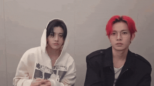 two young men with red hair are sitting next to each other in front of a wall .