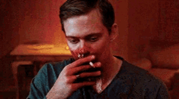 a man with blood on his face is smoking a cigarette and has blood on his face .