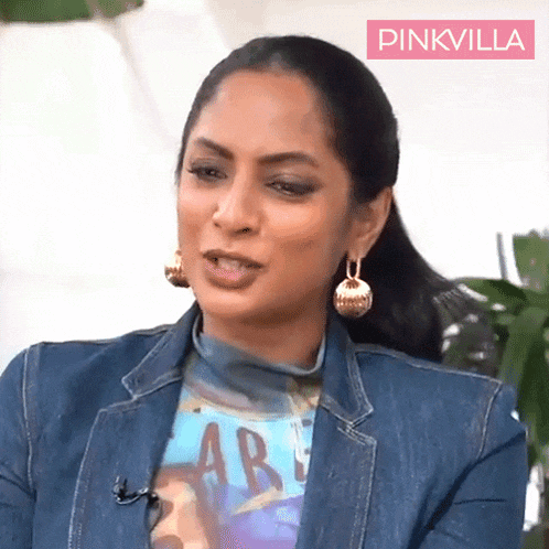 a woman wearing a denim jacket and earrings is sitting in front of a pink villa sign .