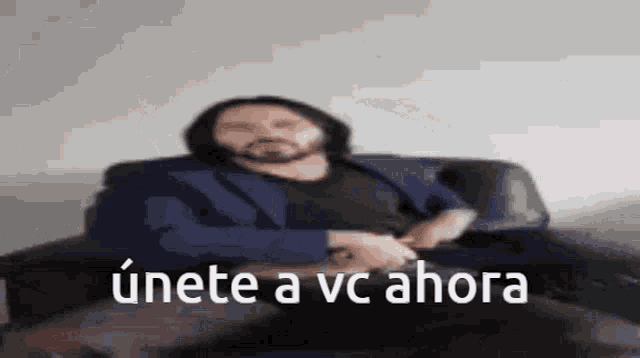 a man with a beard is sitting on a couch with the words " unete a vc ahora " below him