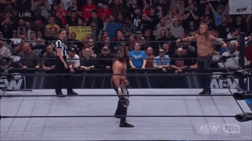 a group of wrestlers are standing in a wrestling ring with a referee and a crowd watching .