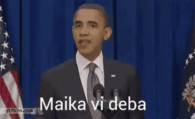 a man in a suit and tie stands at a podium with the words " maika vi deba " written on it