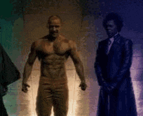 a man without a shirt is standing in front of two men in suits .