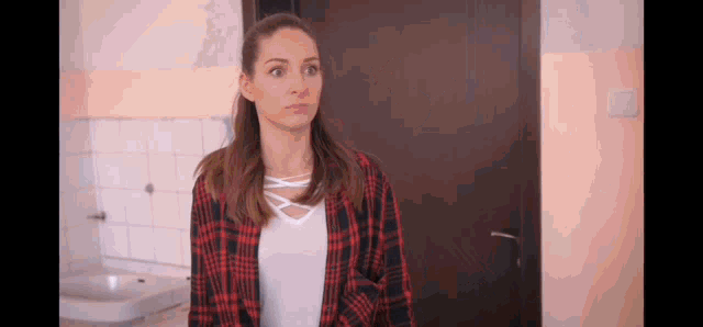 a woman in a plaid shirt is standing in front of a door in a kitchen .