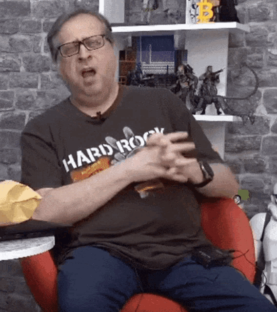 a man wearing a hard rock t-shirt is sitting in a red chair .
