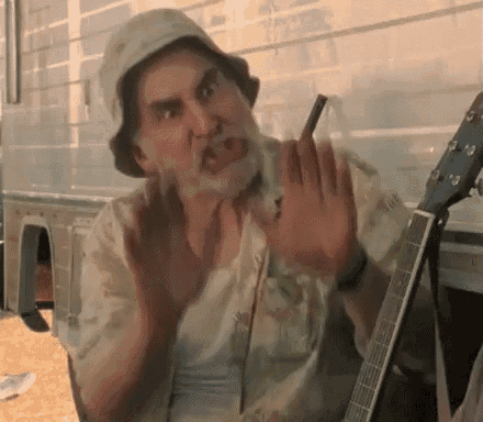 a man with a beard and a hat is holding a guitar and making a funny face .