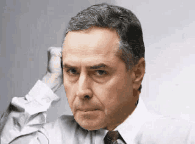 a man in a white shirt and brown tie scratches his head
