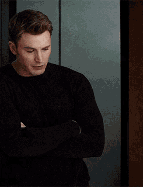 a man wearing a black sweater is standing with his arms crossed