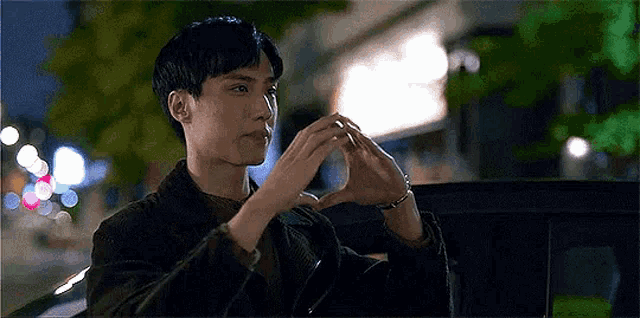 a young man is making a heart shape with his hands while sitting in a car .