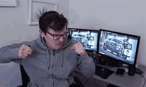 a man sitting in front of two computer monitors one of which has a military vehicle on it