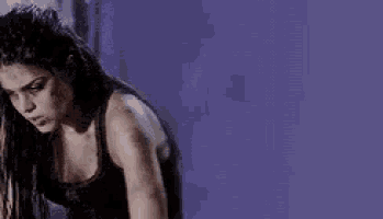a woman in a black tank top is kneeling down in front of a purple wall .