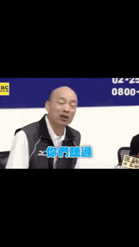 a bald man is sitting in front of a sign that says bbc