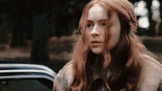a woman with red hair is sitting in a car and looking at the camera .