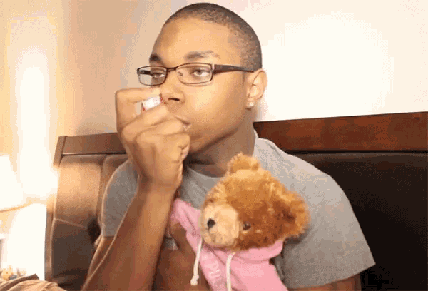 a man wearing glasses is holding a teddy bear and using a nasal spray