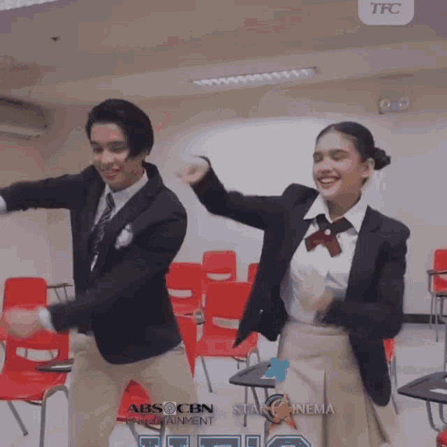 a man and a woman are dancing in a classroom with abs cbn written on the wall