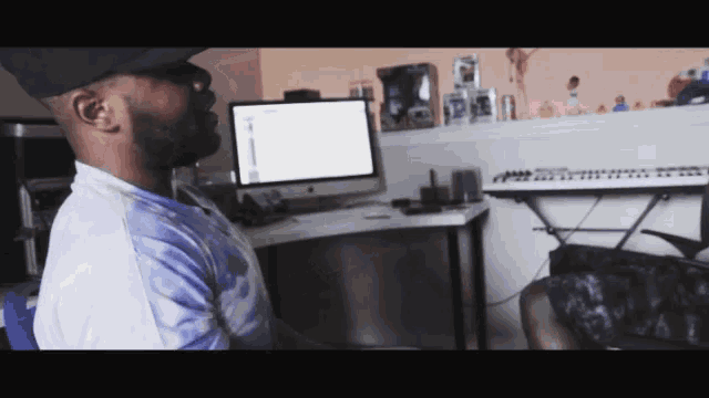 a man in a hat sits in front of a computer and keyboard