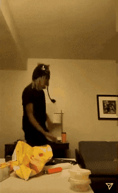 a man wearing a headset stands in a living room with a bag of chips on the table