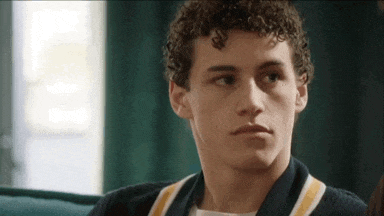 a young man with curly hair is sitting on a couch and looking at something .