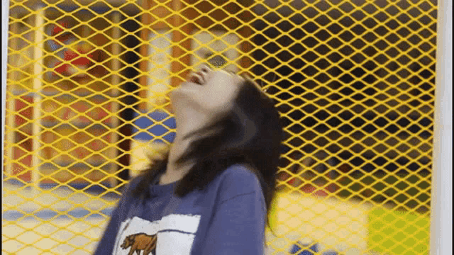 a girl is standing in front of a yellow fence looking up