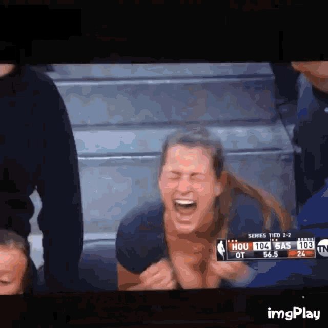a woman is laughing while watching a basketball game on a tv screen