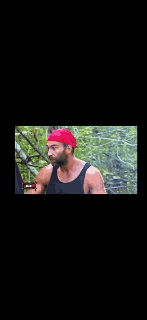 a man with a beard wearing a red headband is standing in the woods .