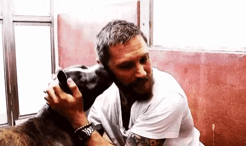 a man with a beard is kissing a dog on the nose .