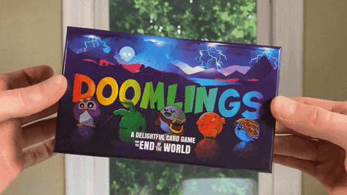 a person is holding a box of doomlings a delightful card game