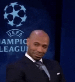 a man in a suit and tie is smiling while sitting in front of a sign that says uefa champions league .