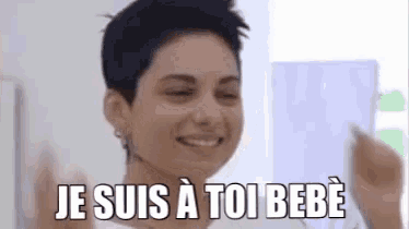 a woman with short hair is smiling and holding a piece of paper with the words je suis a toi bebe on it .