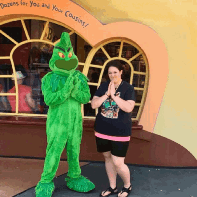 a woman stands next to a grinch mascot in front of a store that says dozens for you and your cousins