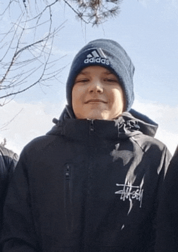 a young boy wearing a black adidas jacket and a beanie