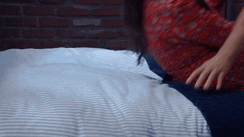 a woman in a red shirt is laying on a bed with a striped blanket