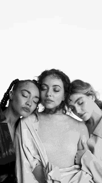 three women are posing for a black and white photo with their eyes closed .
