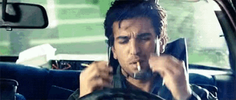 a man is sitting in a car smoking a cigarette and talking on a cell phone .