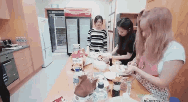 three women are preparing food in a kitchen with a coca cola refrigerator behind them