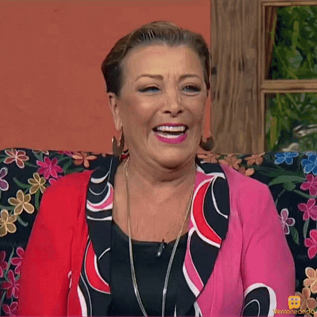 a woman is sitting on a couch with flowers on it and smiling