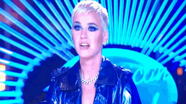 a woman wearing a blue leather jacket and a chain necklace is standing in front of a blue background .
