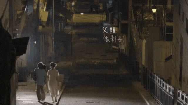 a couple walking down a dark street with chinese writing on the sidewalk