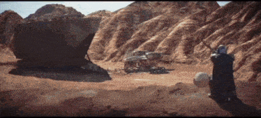 a man is kneeling down in a desert with a sword in his hand .
