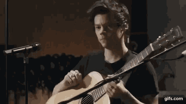 a man is playing an acoustic guitar in front of a microphone and scratching his head .
