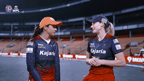 two women wearing kajaria shirts are standing next to each other on a field