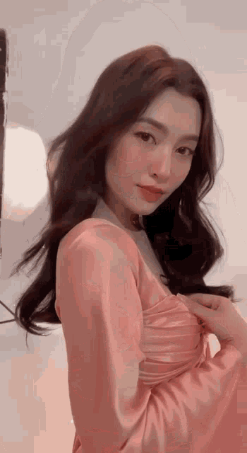 a woman in a pink dress is standing in front of a white wall .