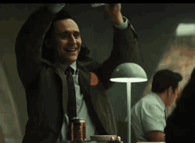 a man in a suit and tie is laughing while standing in front of a lamp .
