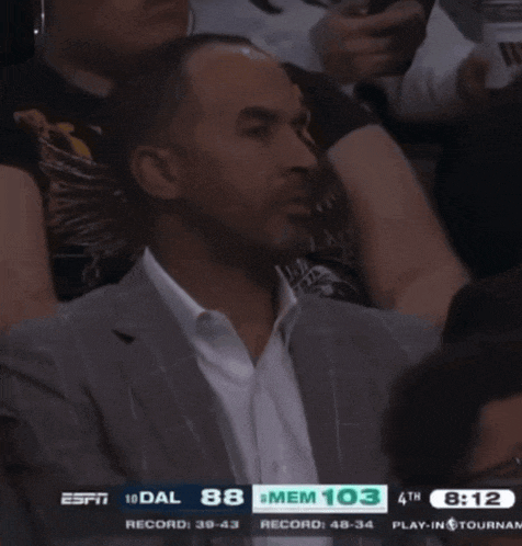 a man in a suit sits in the stands watching a basketball game with espn on the screen