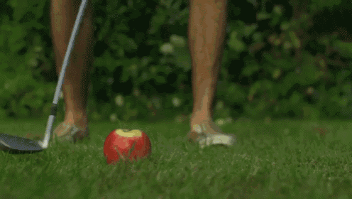 a man is swinging a golf club at an apple that has fallen on the grass